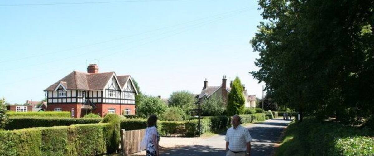 A rural road with a house on the left and a tree-lined path.