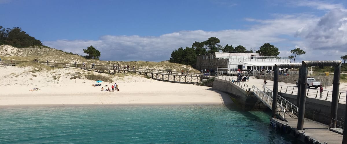 A beach with a wooden pier and a white building in the background.