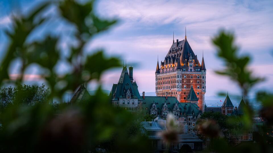A historic building with a pointed roof and multiple spires, surrounded by trees.