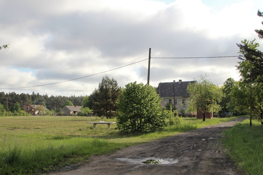 Een landweg met een onverharde weg, omringd door groen en huizen.
