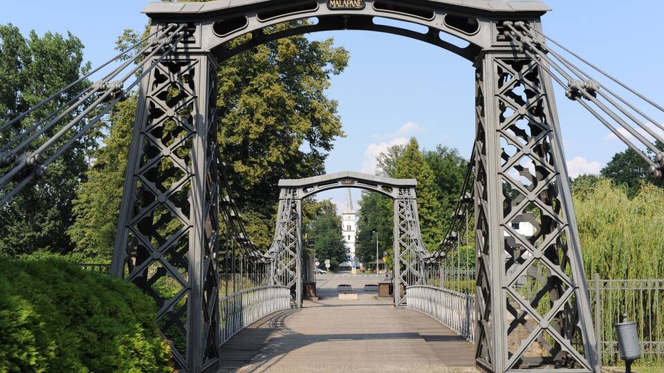 A metal bridge with a sign reading "MALAPANE" and a tower in the distance.