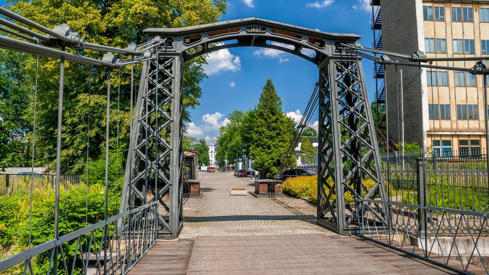 A metal bridge with a date plaque, surrounded by greenery and buildings.