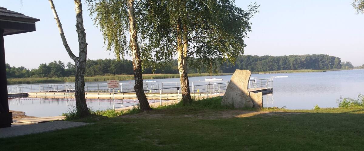 A lakeside park with a wooden pier, trees, and a grassy area.