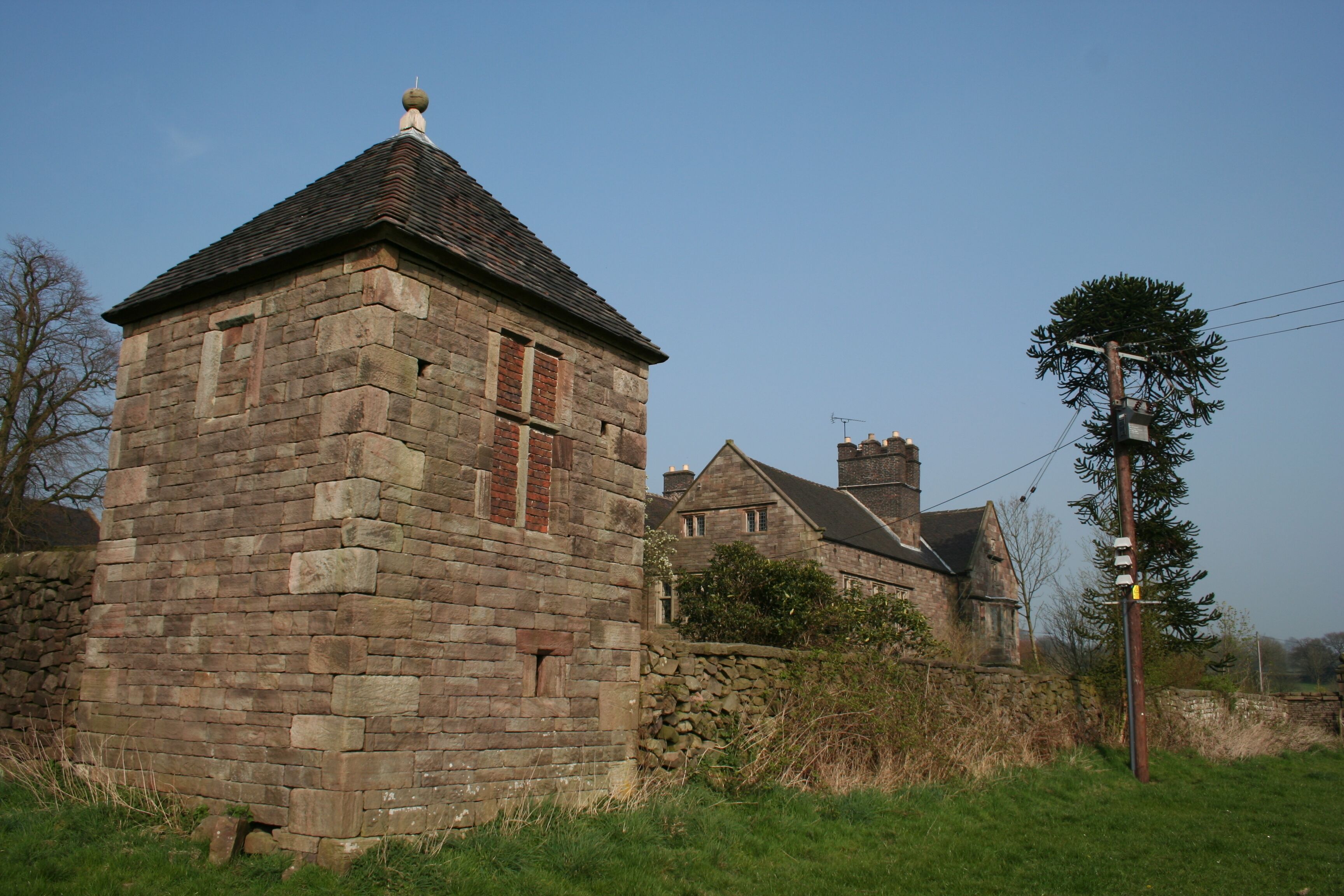 A stone building with a pointed roof, surrounded by grass and a stone wall.