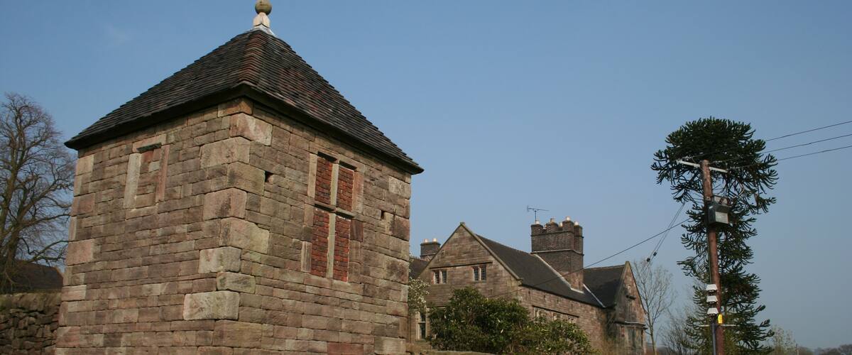 A stone building with a pointed roof, surrounded by grass and a stone wall.