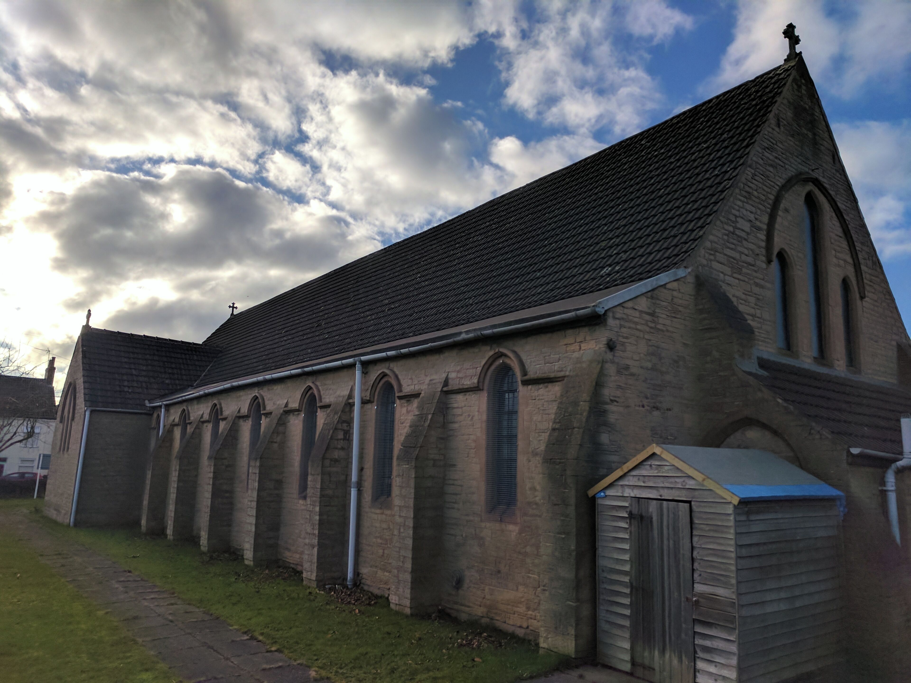 A church with a steeply pitched roof, arched windows, and a small shed to the right.