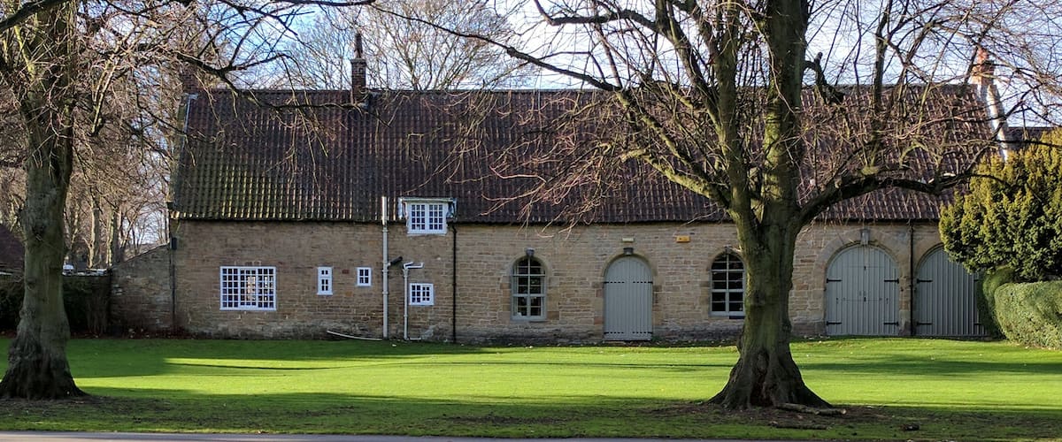 A stone building with a tiled roof, surrounded by a well-maintained lawn and trees.