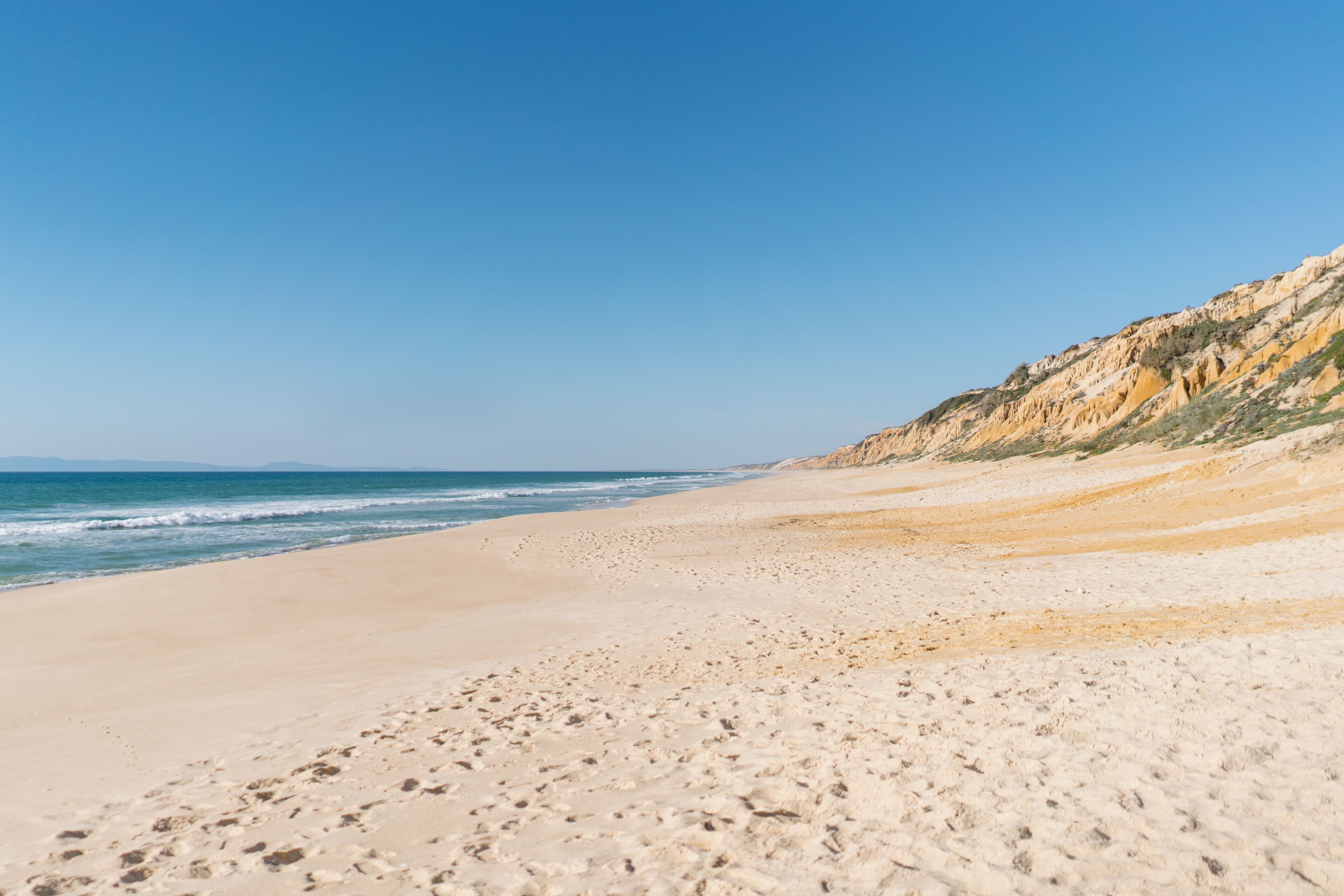 Ein sandiger Strand mit sanften Wellen und einem felsigen Felsen im Hintergrund.