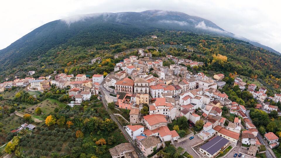 An aerial view of a historic town nestled in a valley with a prominent mountain in the background.