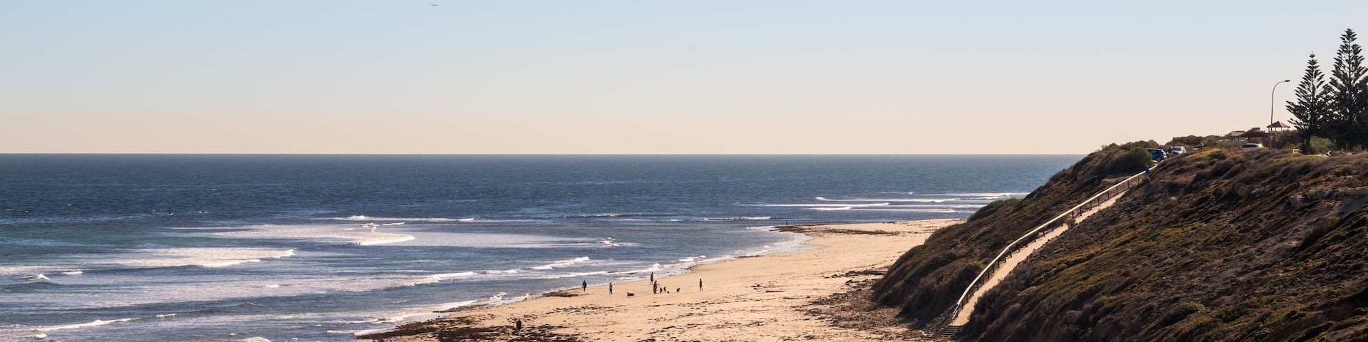 A beach with waves, people, and a coastal path.