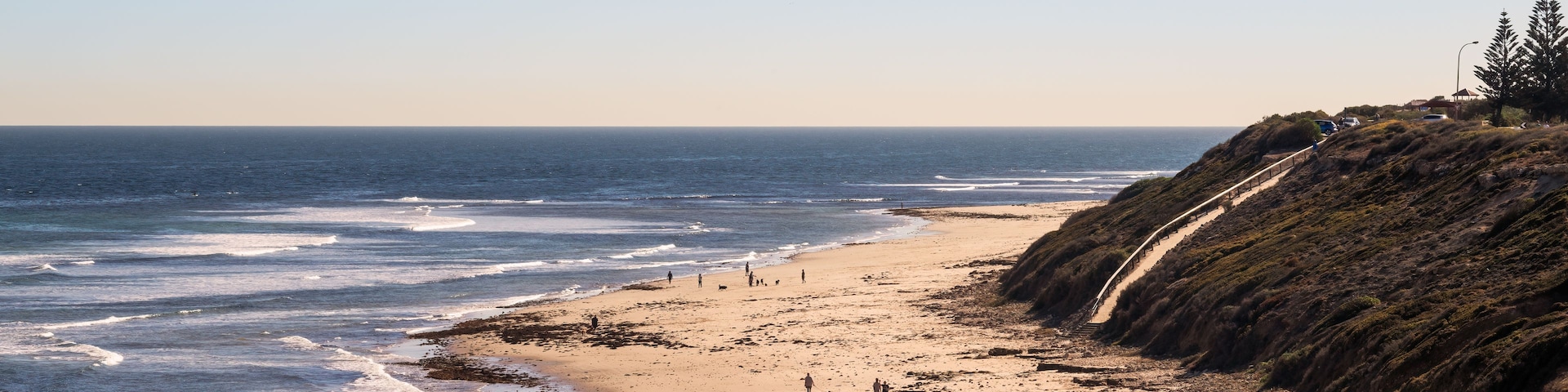 A beach with waves, people, and a coastal path.