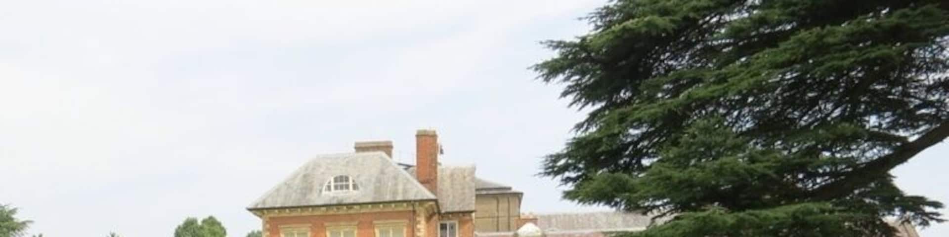 A well-manicured garden with a stone monument, neatly trimmed hedges, and a large brick building in the background.