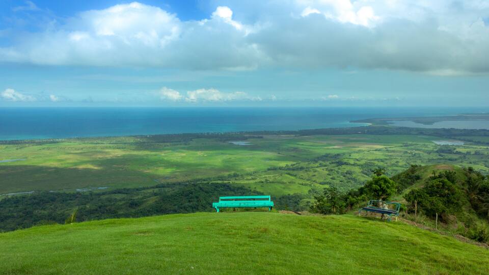 A turquoise bench overlooking a coastal landscape with green fields and the ocean in the distance.