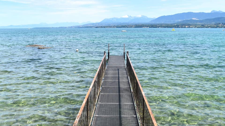 A pier extending into a clear lake with mountains in the background.