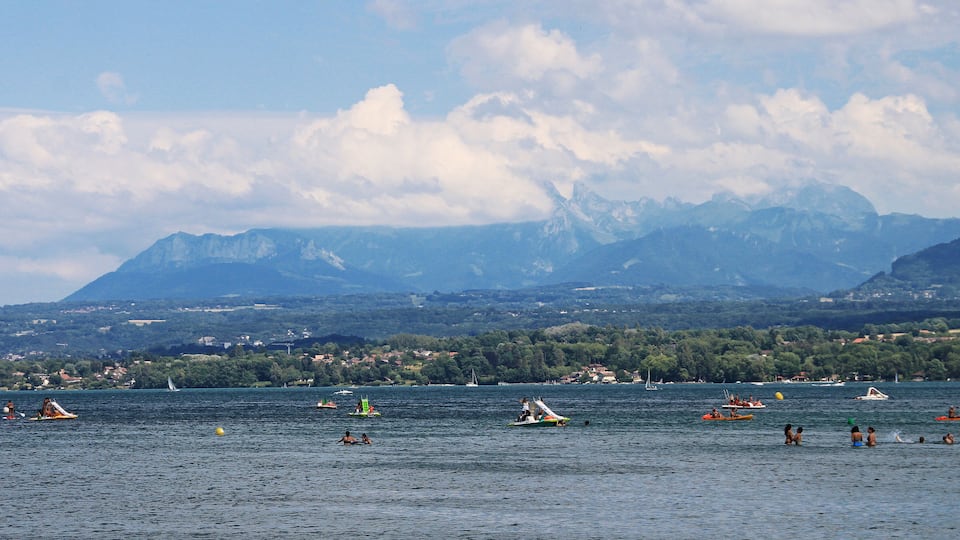 A lake with boats and people, surrounded by mountains and a town in the background.