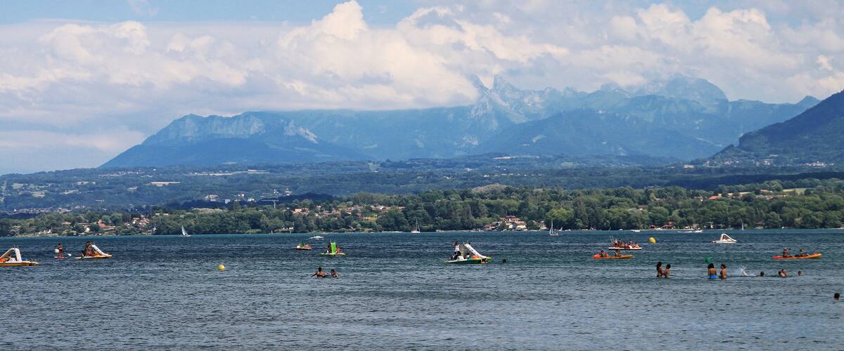 A lake with boats and people, surrounded by mountains and a town in the background.