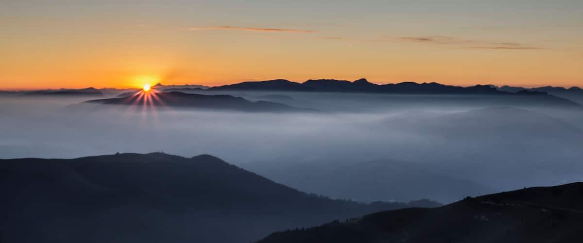 A sunrise over a mountain range with mist-covered peaks.