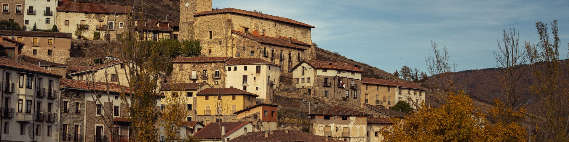 Un pueblo histórico con edificios en una ladera, una torre destacada y follaje otoñal.