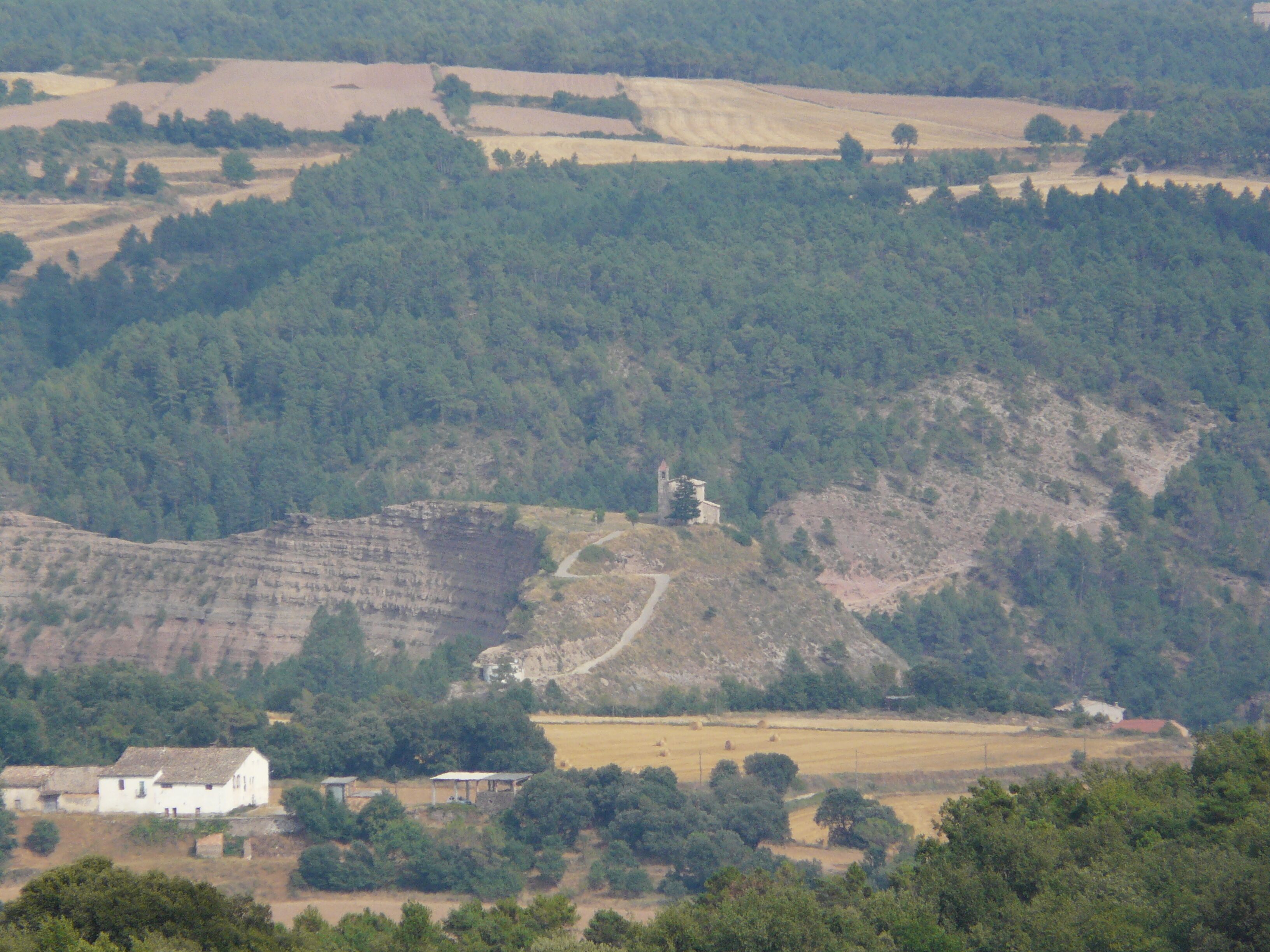 A rural landscape with a church on a hill, surrounded by fields and trees.