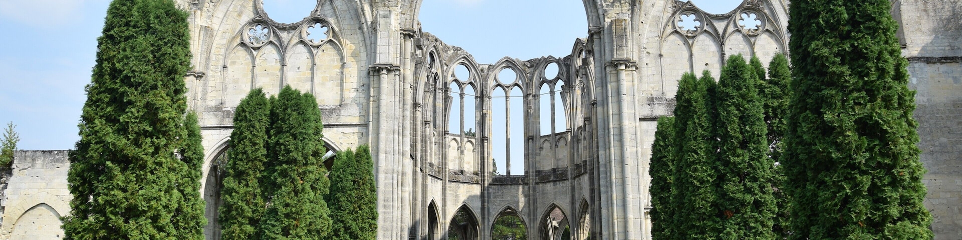 Una catedral gótica con un gran arco, rodeada de árboles siempre verdes bien cuidados.