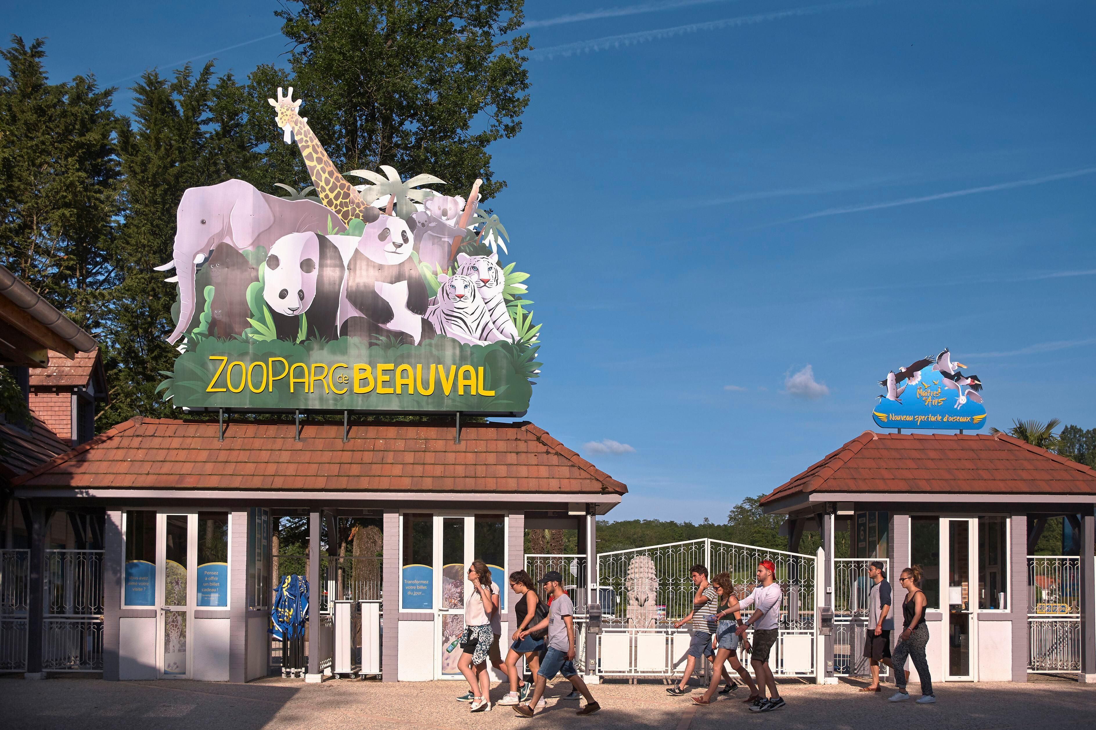A zoo entrance with a sign featuring animals like a giraffe, elephant, and panda.