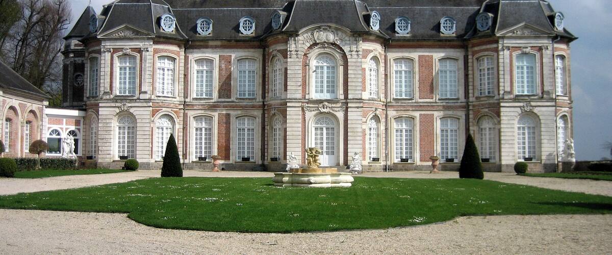 A large, historic building with a symmetrical facade, multiple windows, and a central courtyard with a fountain.