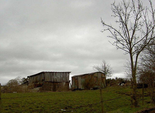 Two old, weathered barns on a grassy hill under a cloudy sky.