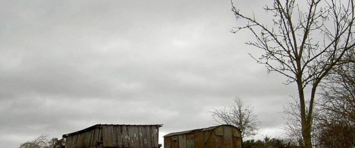 Two old, weathered barns on a grassy hill under a cloudy sky.