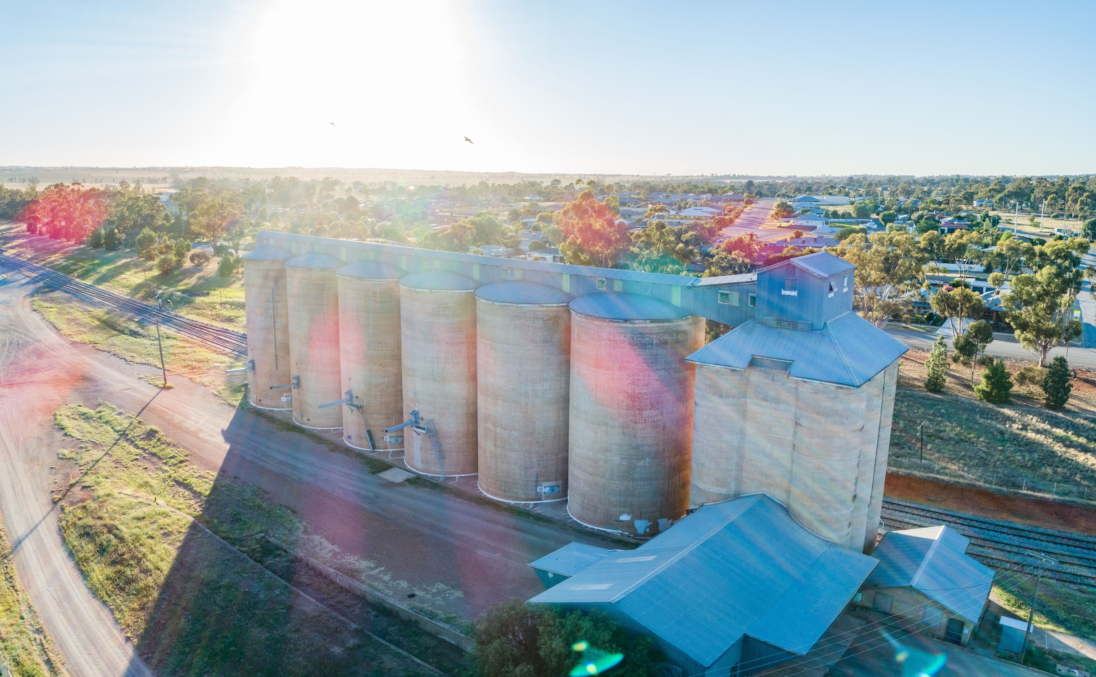 Morning sunlight shining over wheat silo infrastructure beside a train line in the riverina
