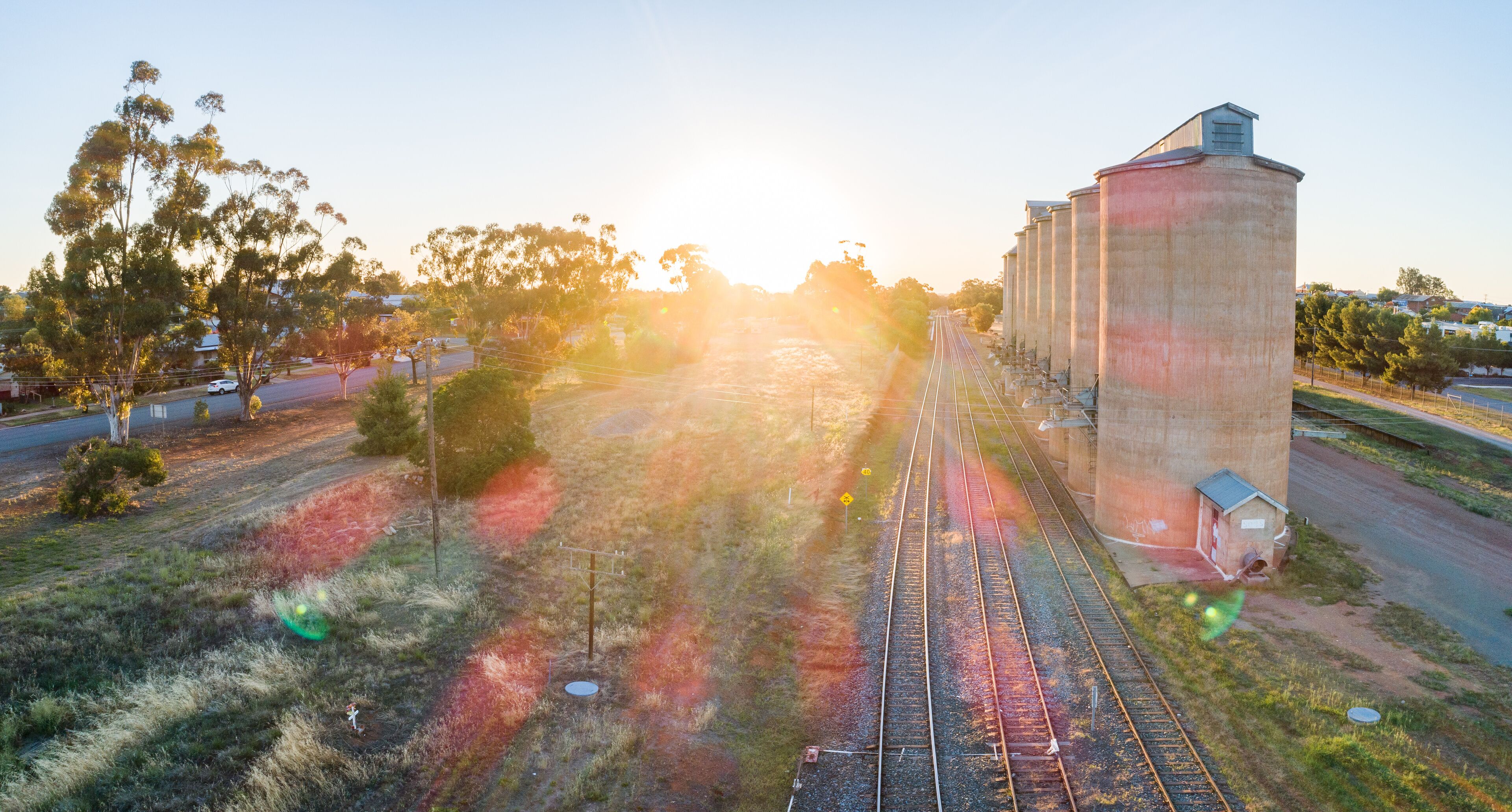 Golden sun flare over landscape aerial view of grain silos beside train line