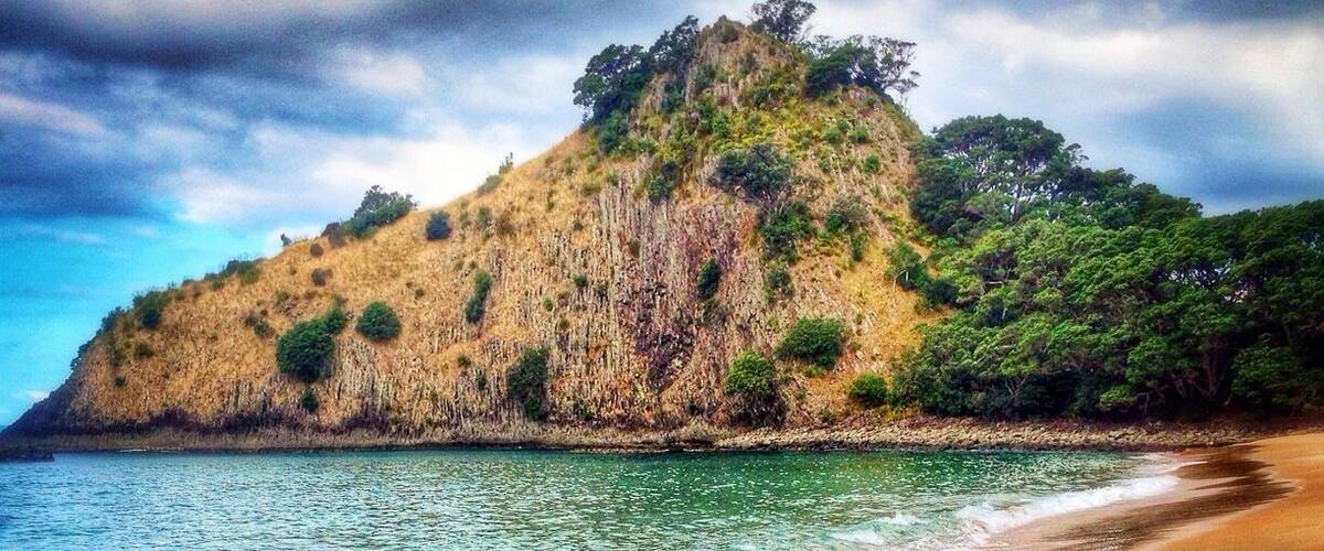 Una playa arenosa con un acantilado rocoso y abundante vegetación.