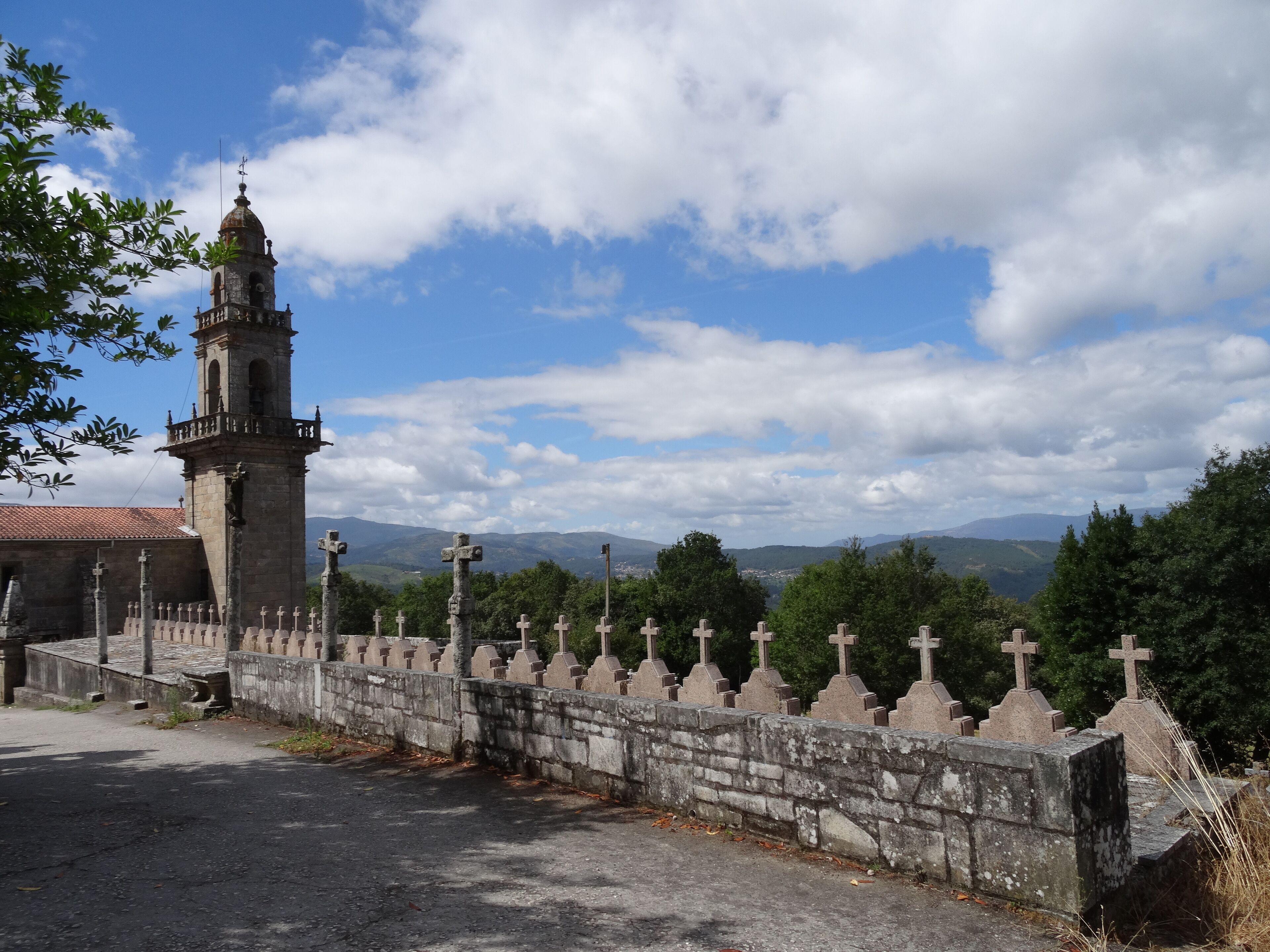A stone wall with crosses, a church tower, and a mountainous landscape in the background.