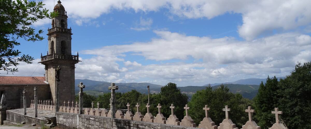 A stone wall with crosses, a church tower, and a mountainous landscape in the background.