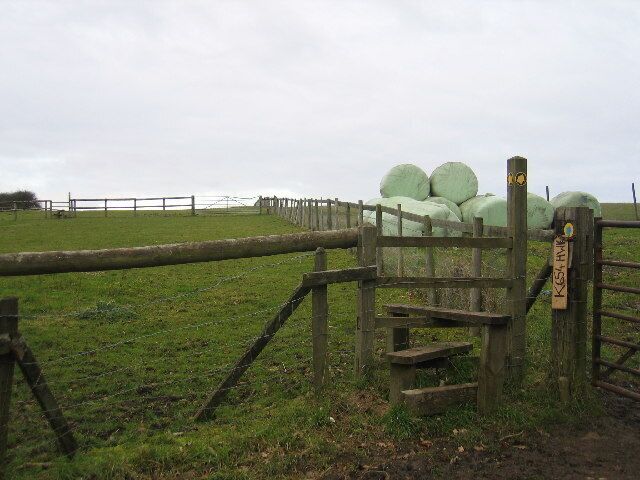 A rural landscape with a wooden gate, hay bales, and a grassy field.