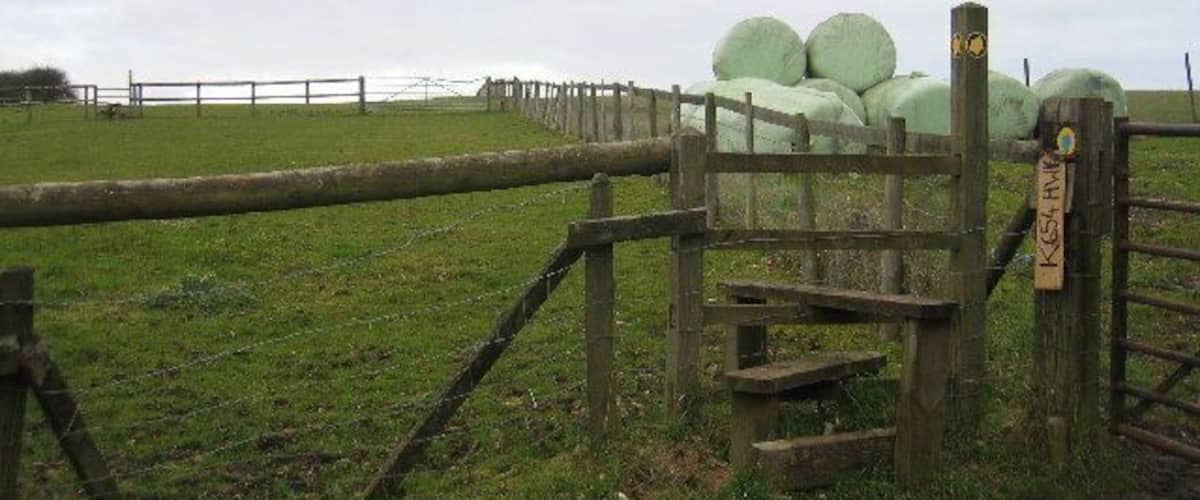 A rural landscape with a wooden gate, hay bales, and a grassy field.