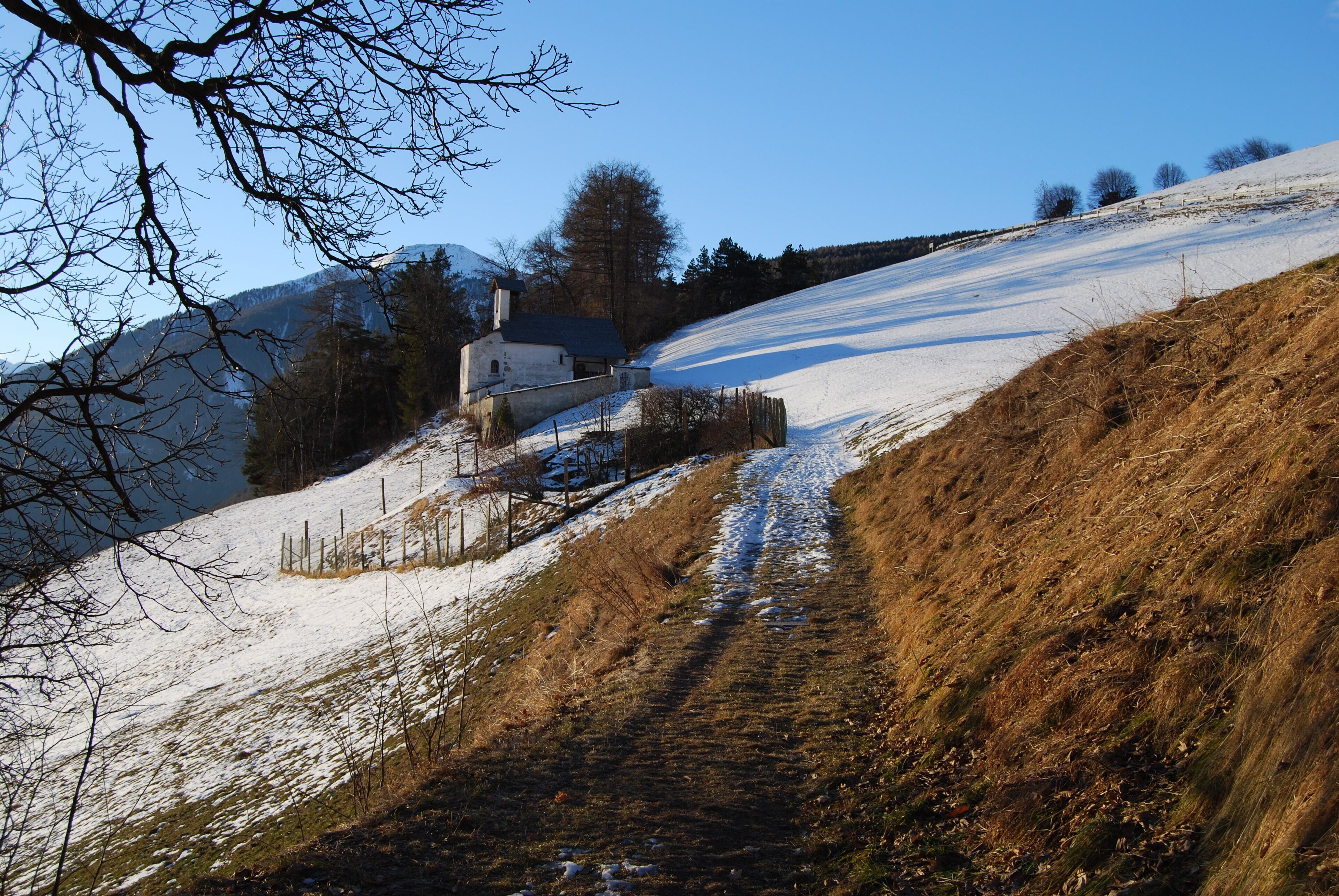 A snow-covered hill with a path leading to a white house.