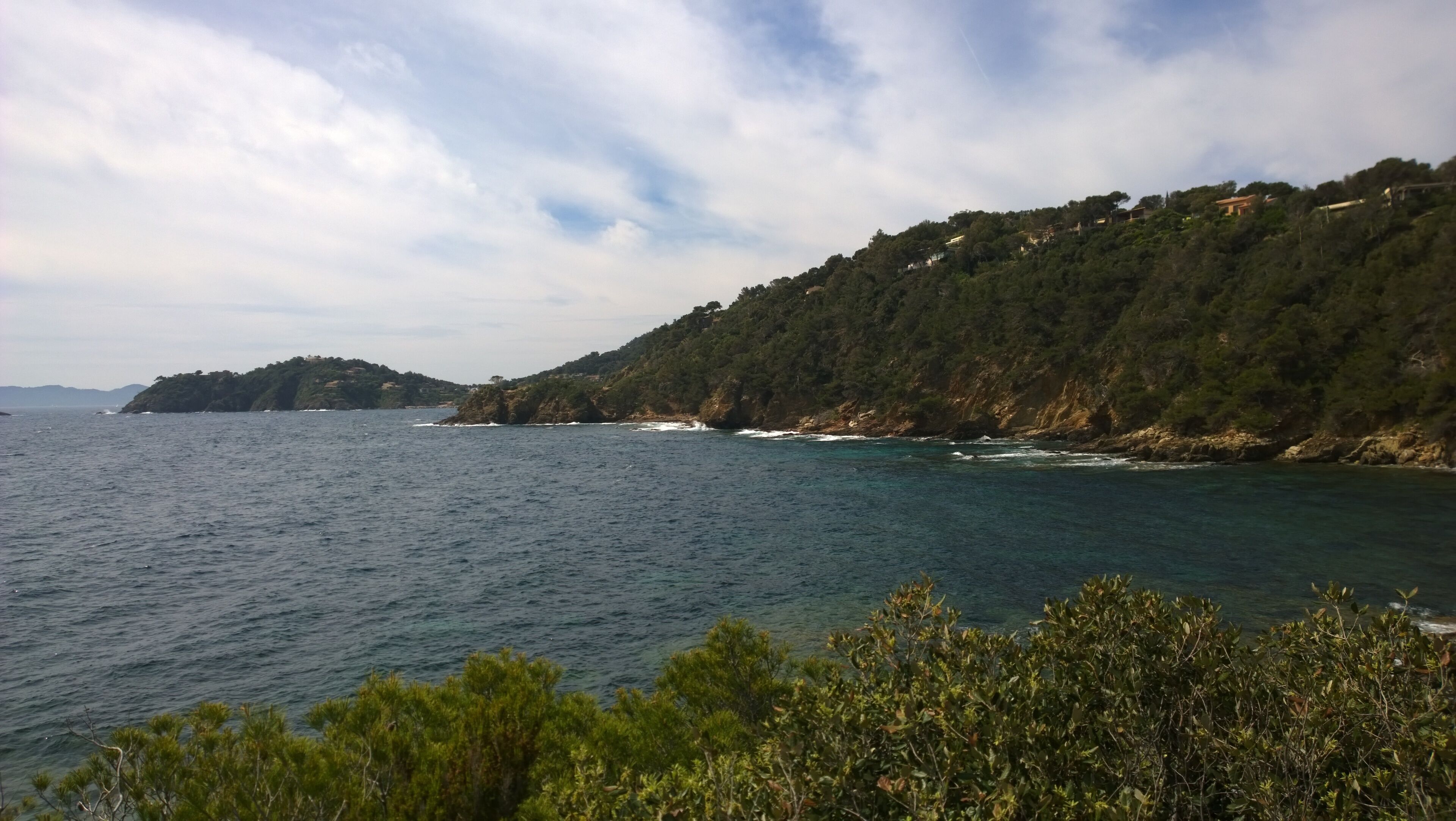 Un paisaje costero con vista despejada al mar, una colina boscosa y montañas distantes.