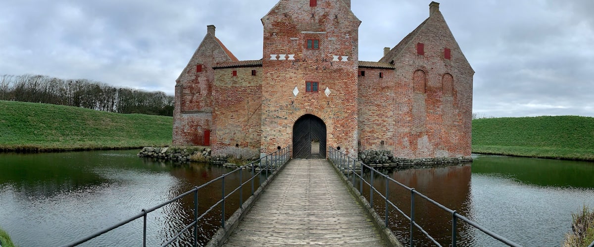 A historic brick tower with a drawbridge over a calm river.