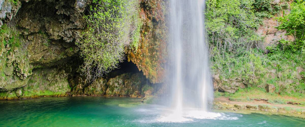 A waterfall cascading into a clear, turquoise pool surrounded by rocky cliffs and lush greenery.