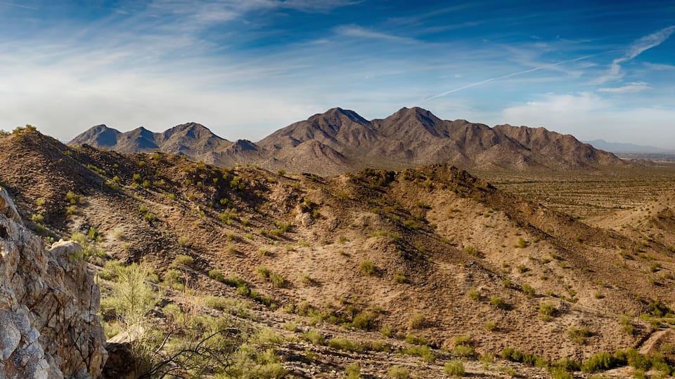 A mountainous landscape with sparse vegetation and a distant city.