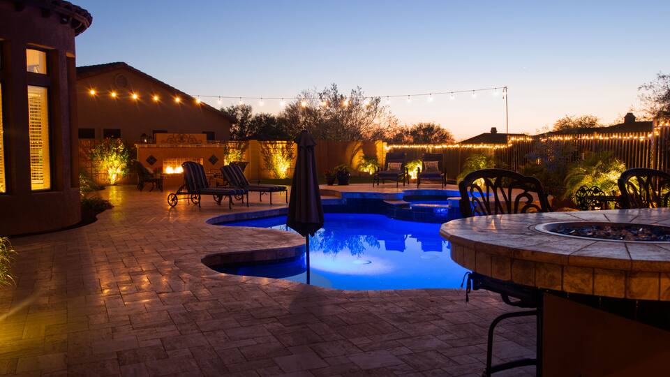 A backyard with a swimming pool, lounge chairs, and string lights.