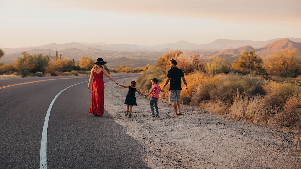 A family walking on a road with a desert landscape and mountains in the background.