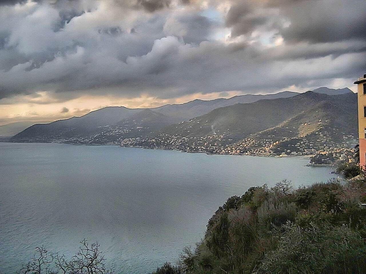 A coastal town with mountains in the background and a cloudy sky.