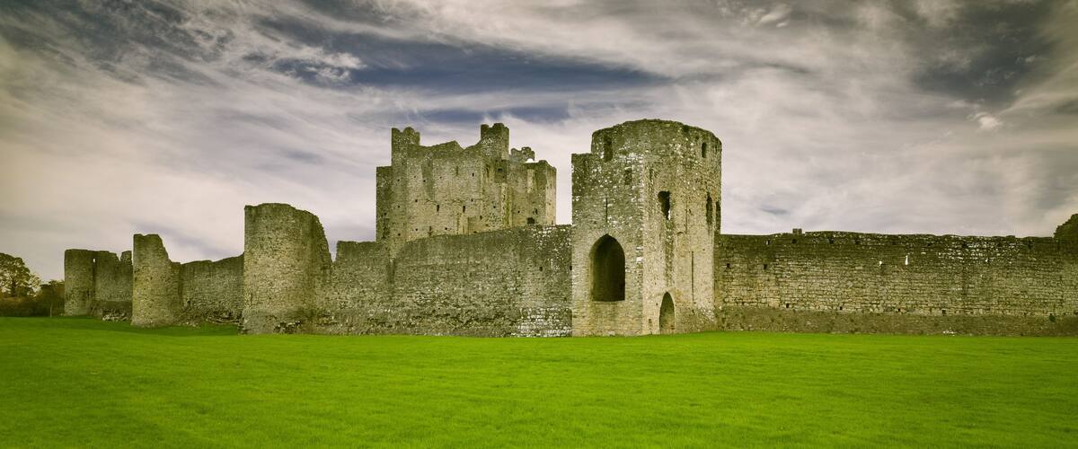 A historic castle with multiple towers and a large grassy field in front.