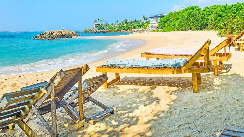 A beach with wooden lounge chairs and a clear view of the ocean.
