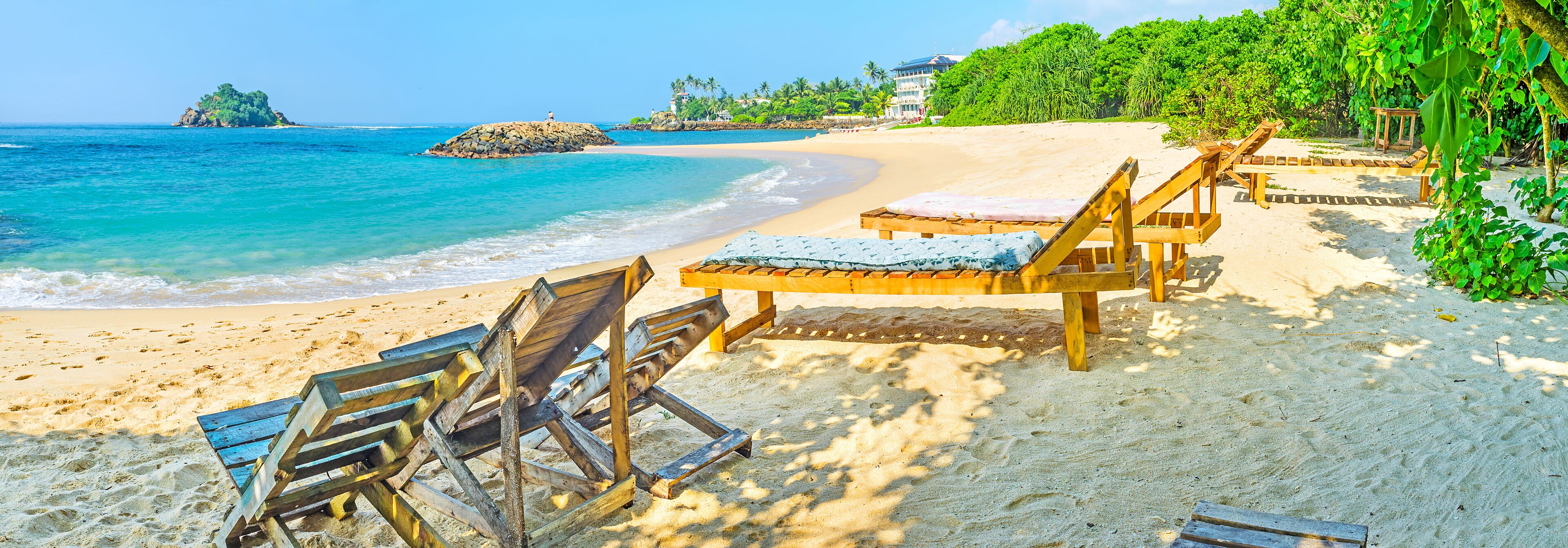 A beach with wooden lounge chairs and a clear view of the ocean.