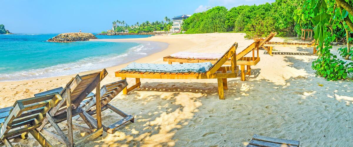 A beach with wooden lounge chairs and a clear view of the ocean.