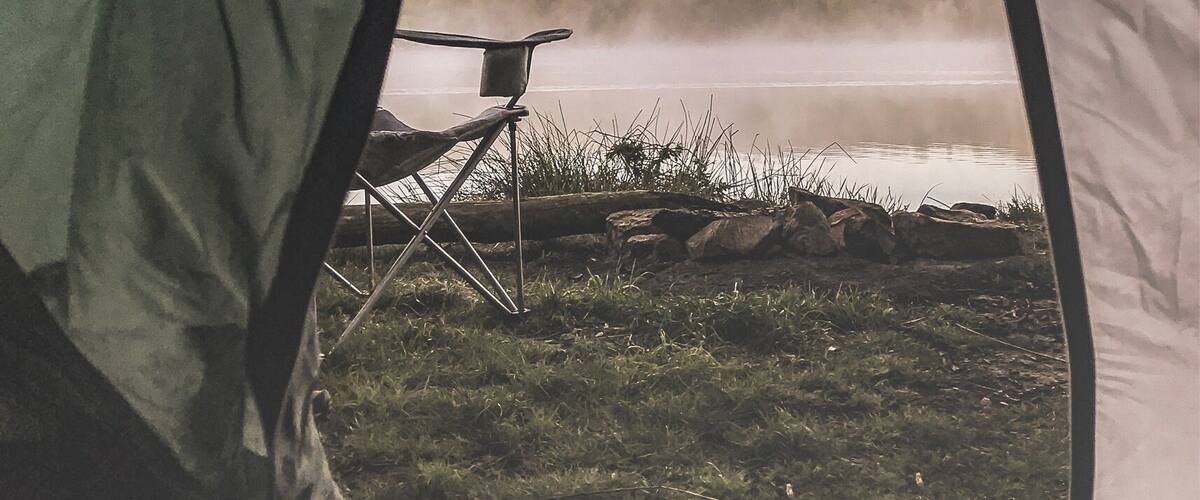A tent with a view of a lake and a chair.