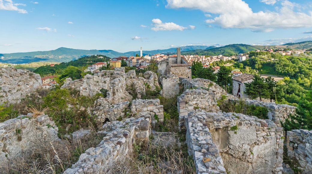 Eine historische Steinruine mit Blick auf eine Stadt und Berge im Hintergrund.