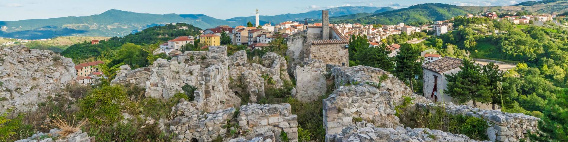 A historic stone ruin with a view of a town and mountains in the background.